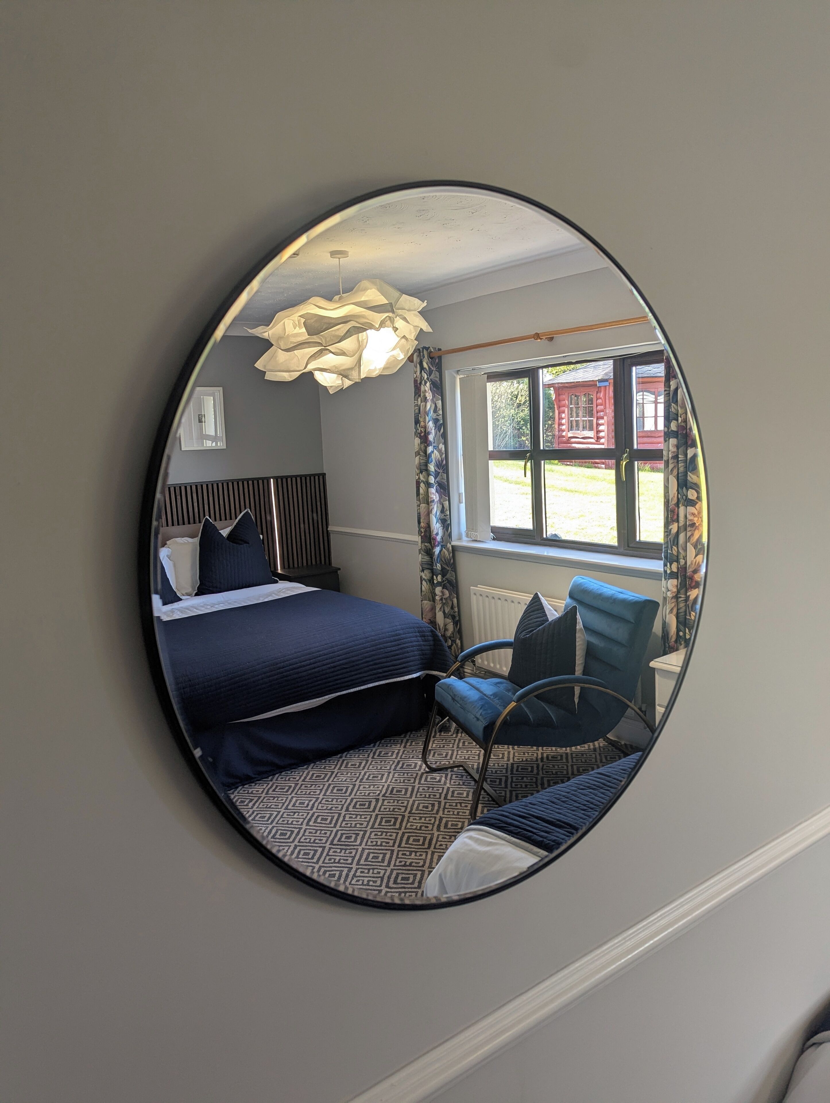 A bedroom with a bed, a chair, a mirror, and a window with curtains.