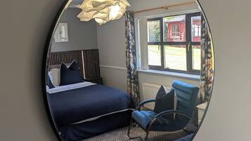 A bedroom with a bed, a chair, a mirror, and a window with curtains.