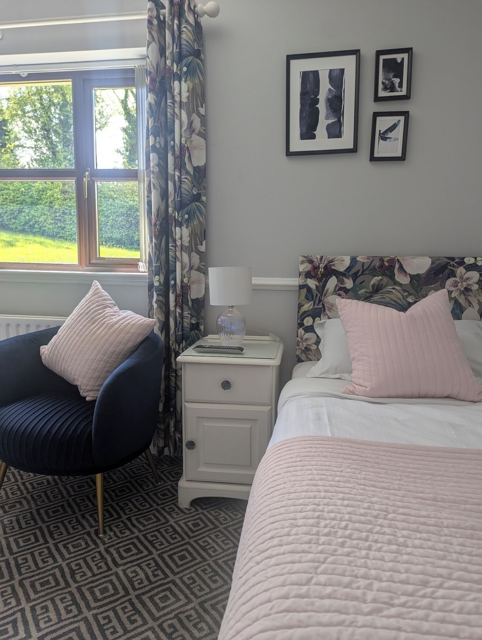 A hotel room with a bed, a chair, a nightstand, and a window with curtains.