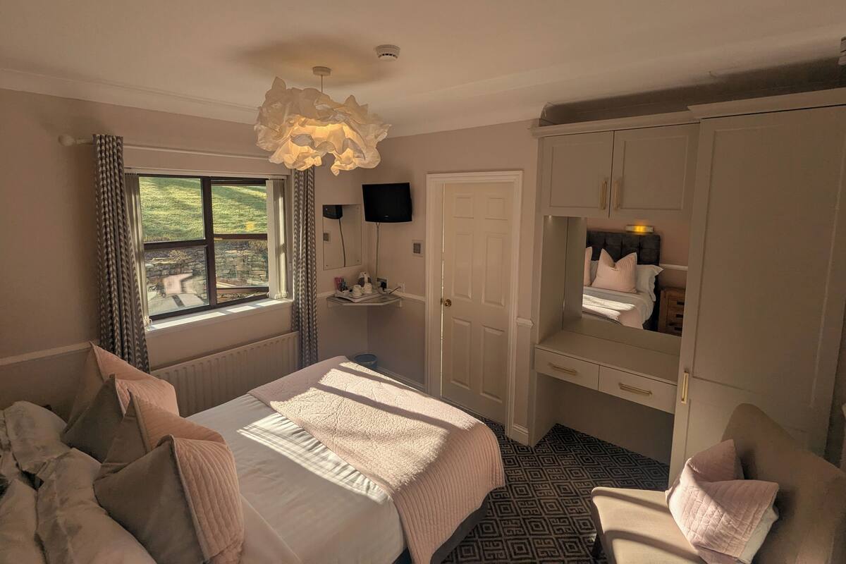 A bedroom with a large bed, a dresser, a TV, and a window with curtains.
