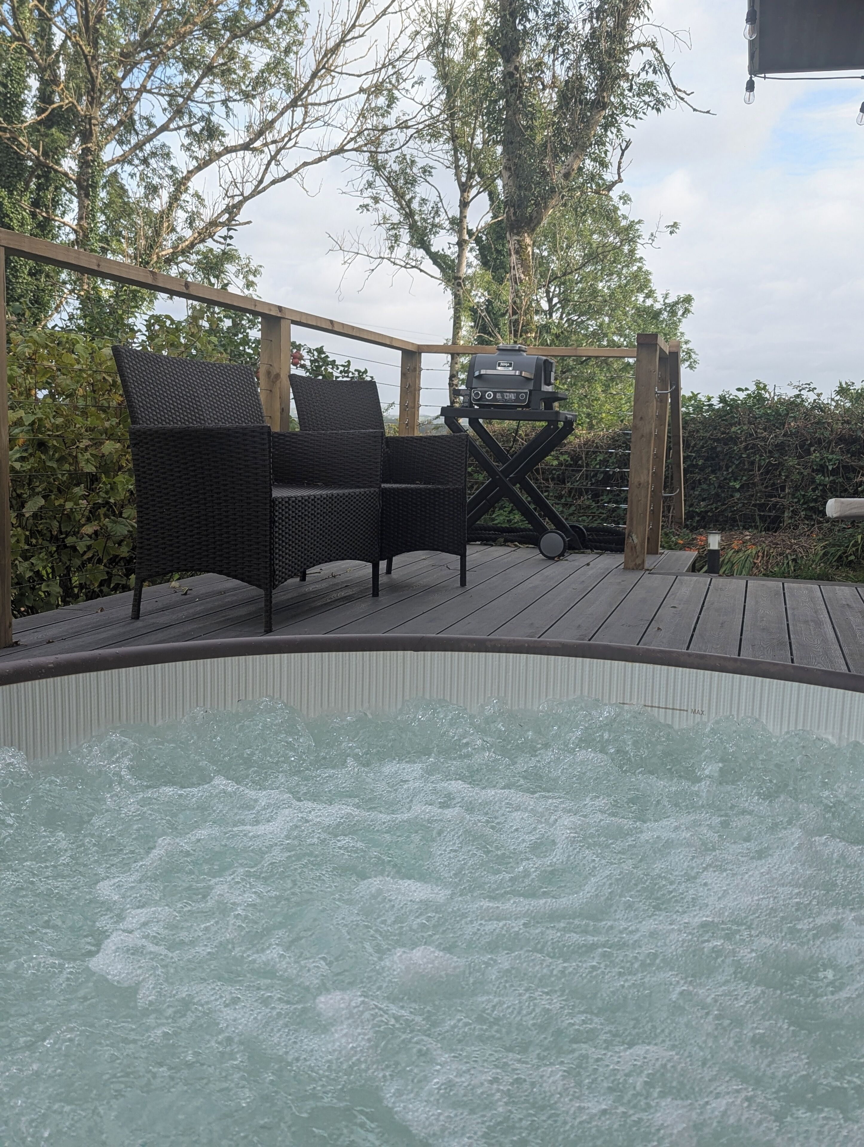 Een hottub met een houten terras, twee rieten stoelen en een barbecue.