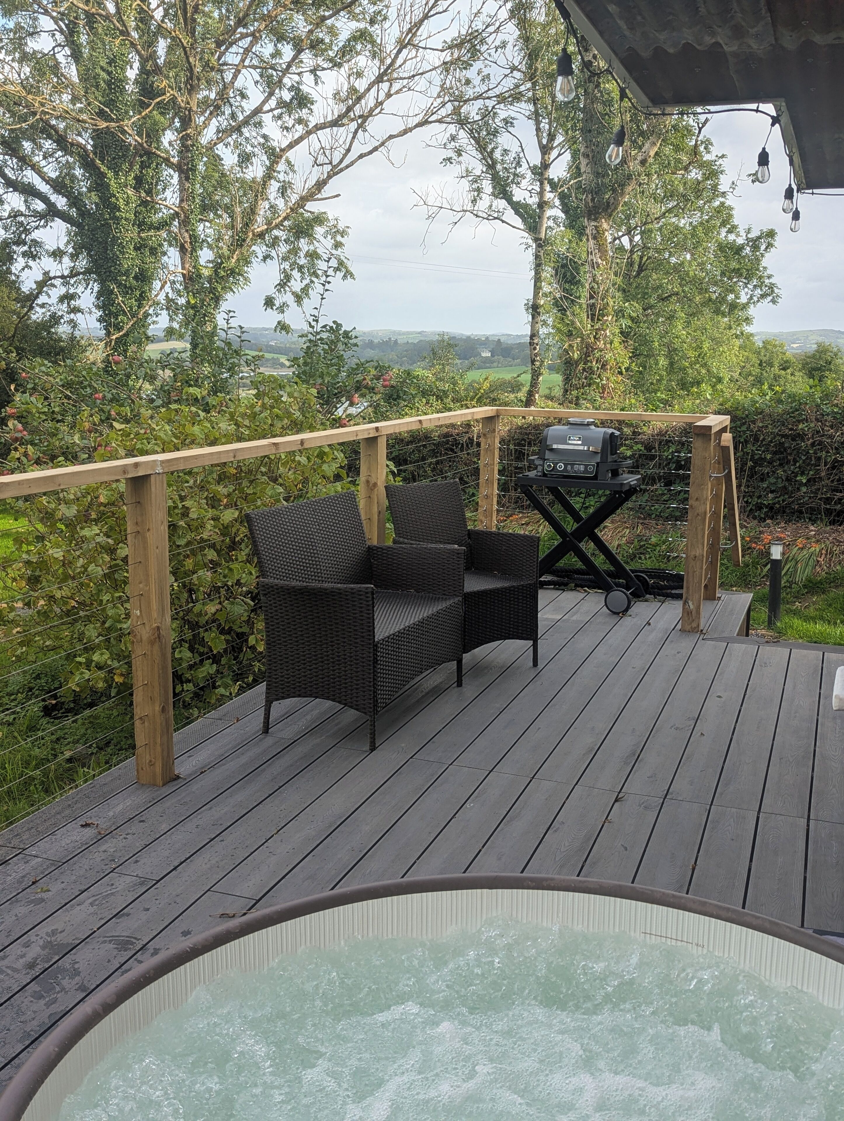 A wooden deck with a hot tub, wicker chairs, and a barbecue grill.