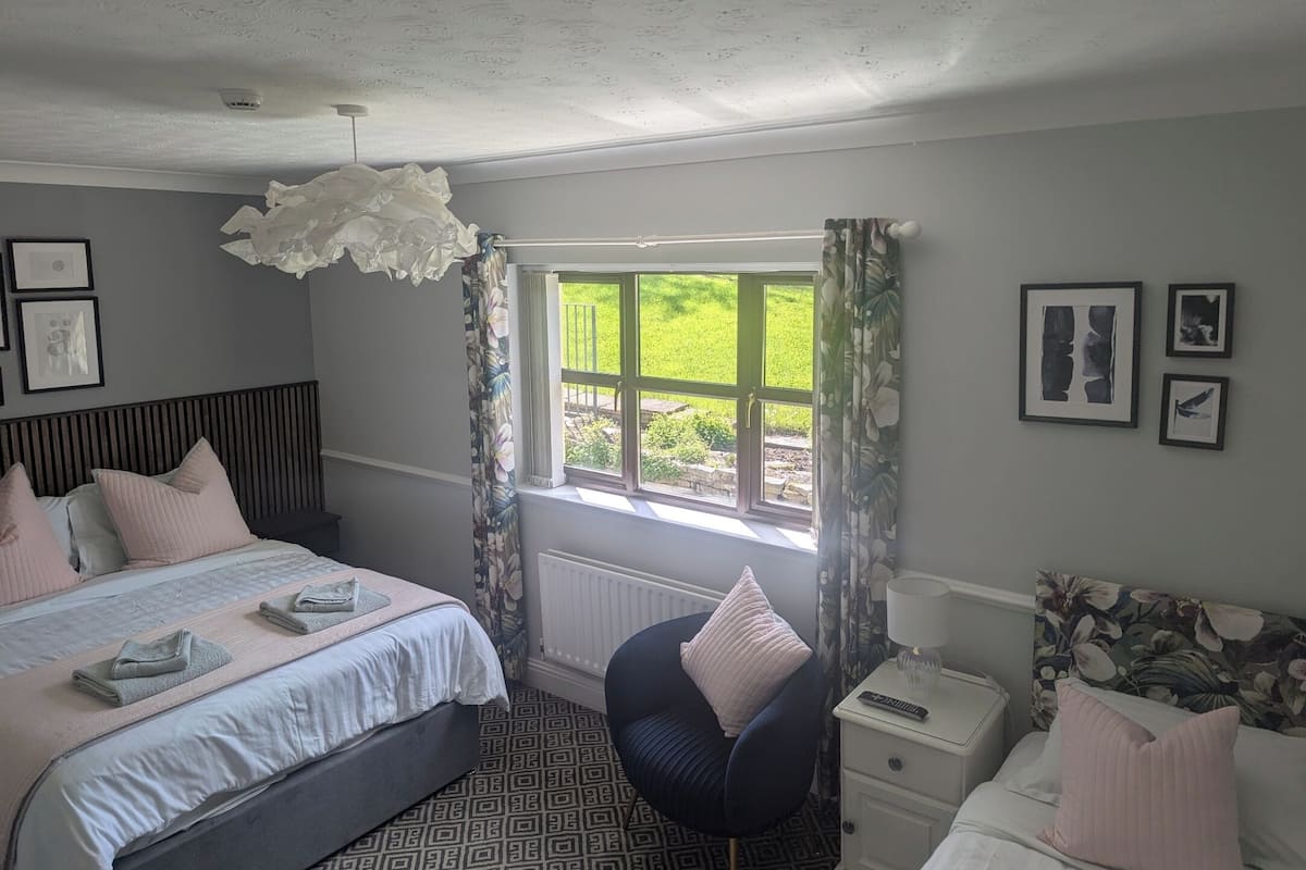A bedroom with a bed, bedside table, chair, and a window with curtains.