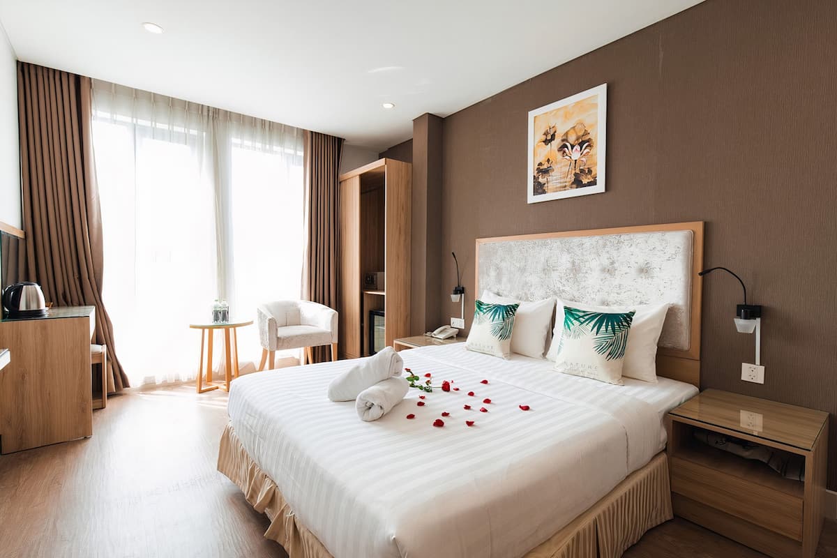 A hotel room with a large bed, a desk, a chair, and a nightstand.