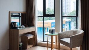 A hotel room with a desk, chair, and large windows offering a view of buildings and trees. - My Villa Hotel Airport (Ho Chi Minh City)