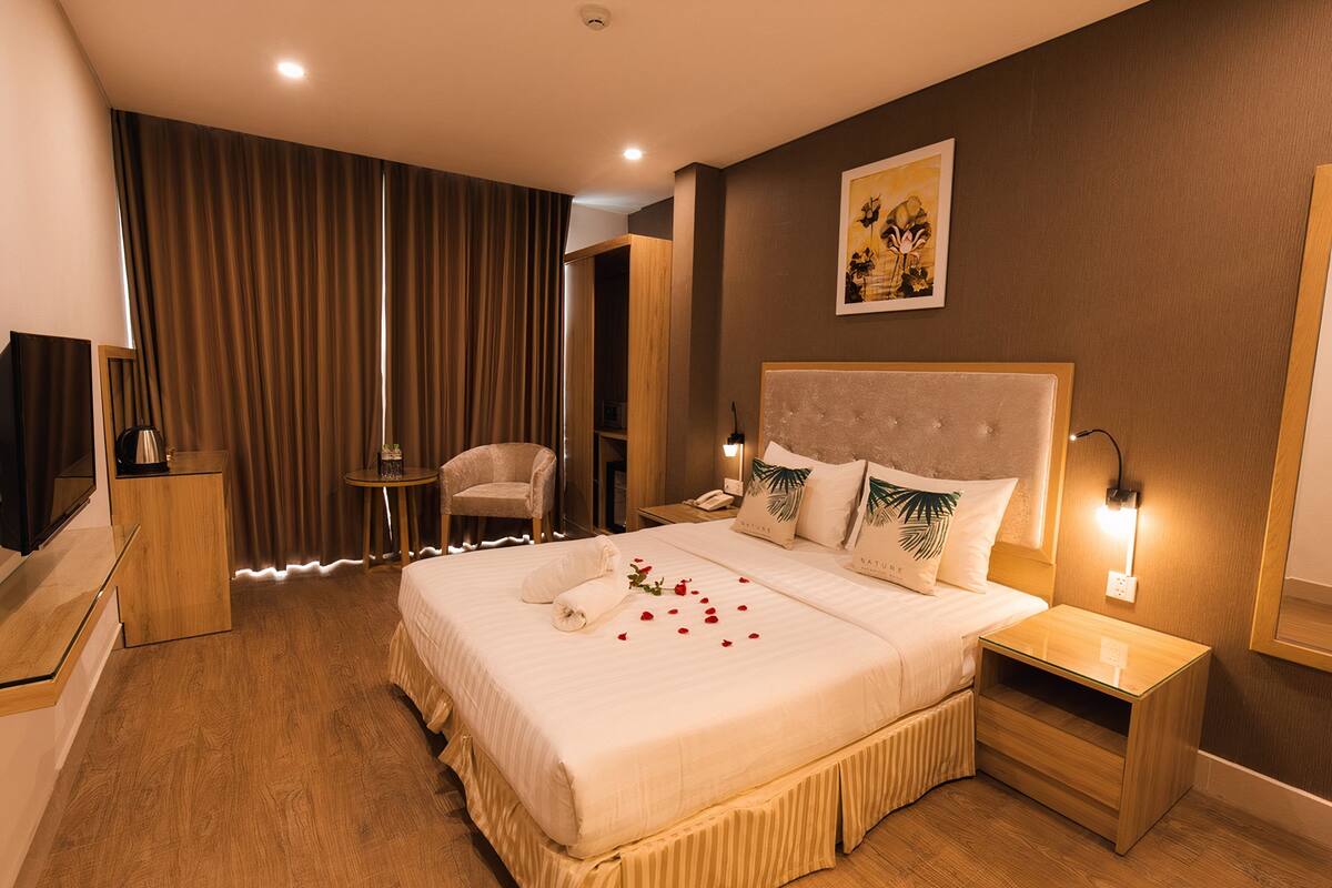 A hotel room with a large bed, a bedside table, a chair, a TV, and a painting on the wall.