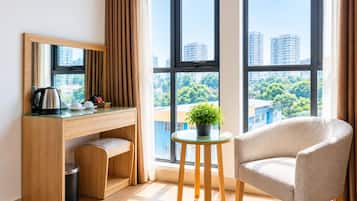 Ein modernes Hotelzimmer mit einem Holztisch, einem Stuhl, einem kleinen Tisch mit Pflanze und großen Fenstern mit Blick auf die Stadt.