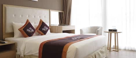 A hotel room with a large bed, a bedside table, a chair, a small table, and a window with curtains.