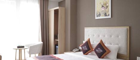 A hotel room with a bed, a bedside table, a chair, a wardrobe, and a painting on the wall.