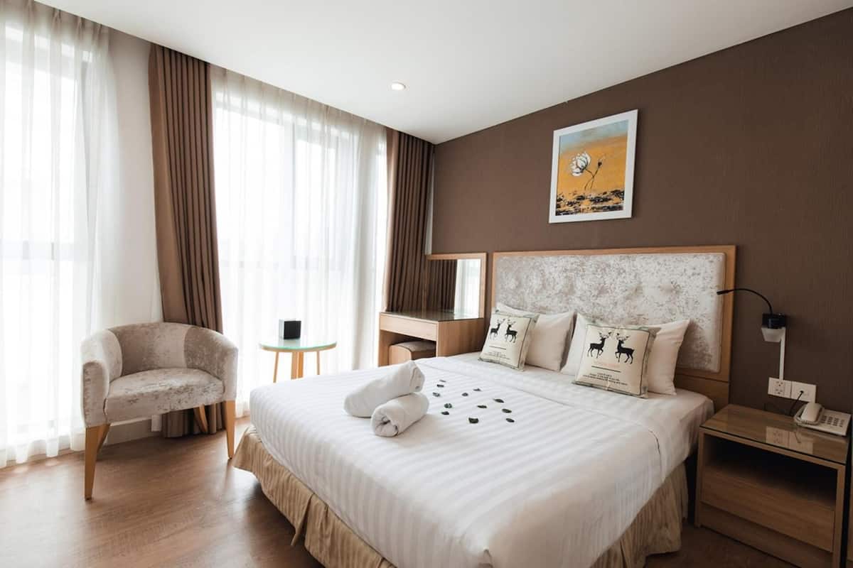 A hotel room with a large bed, a chair, a desk, a nightstand, and a painting on the wall.