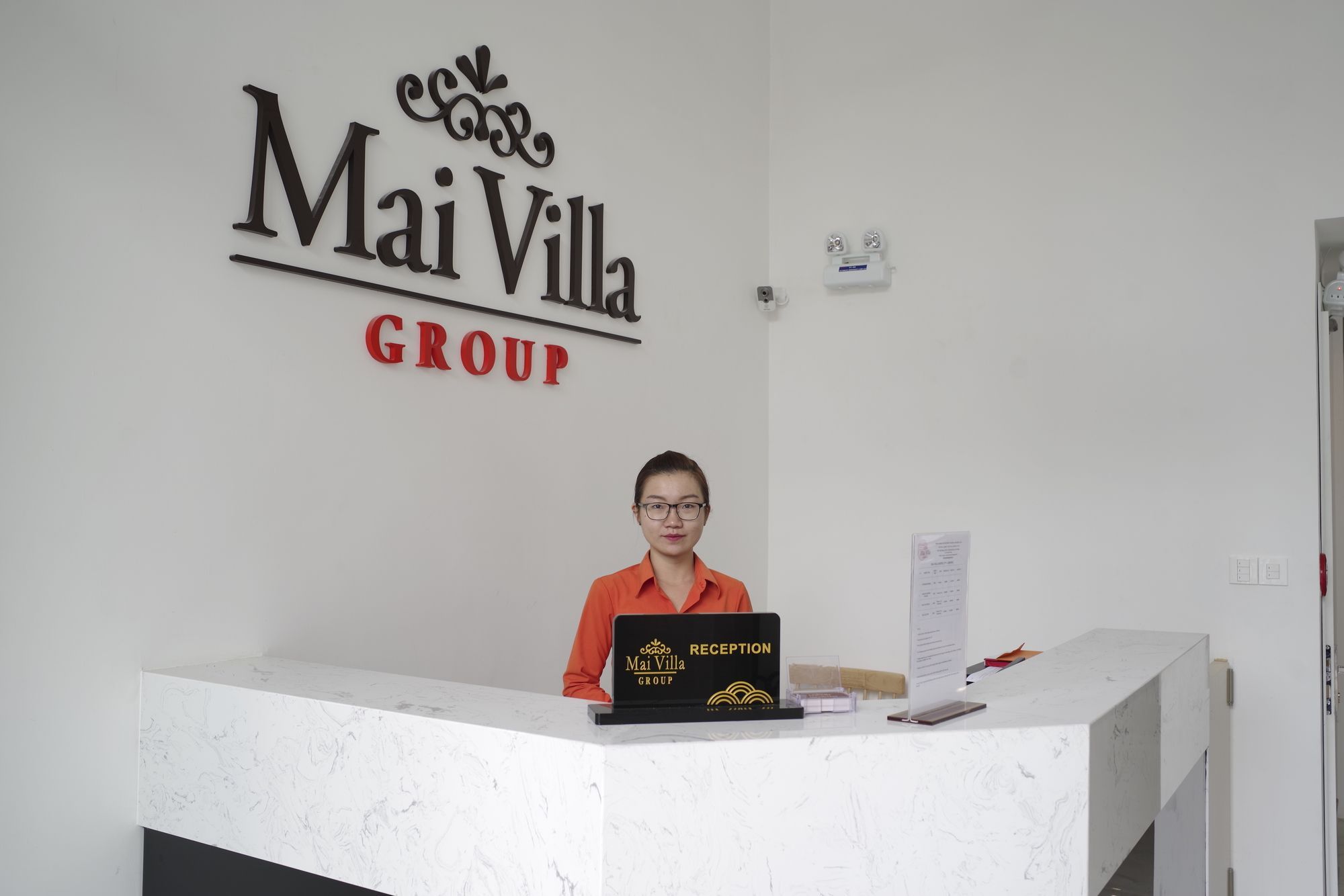 Una mesa de recepción con un cartel que dice 'Mai Villa GROUP' y una persona sentada detrás.