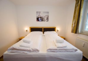 Un lit double avec du linge de lit et des serviettes blanches, une tête de lit en bois, des lampes de chevet, un tableau encadré au mur et une fenêtre avec des rideaux.