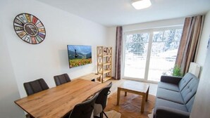 Uma sala de estar moderna com uma mesa de jantar de madeira, sofá de couro e uma grande janela com vista para árvores cobertas de neve.