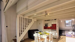 A modern kitchen with red tiles, a dining area with white furniture, and a staircase leading to another level. - Carnac cozy T2 with balcony, pets allowed, private parking (Carnac)