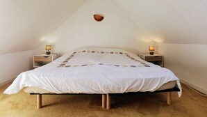 A bedroom with a sloped ceiling, a bed with a white bedspread, two bedside lamps, and a small wall-mounted light fixture. - Carnac cozy T2 with balcony, pets allowed, private parking (Carnac)