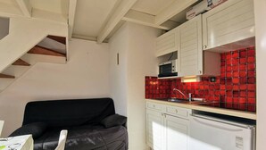 A compact kitchen with white cabinets, a red backsplash, and a black sofa. - Carnac cozy T2 with balcony, pets allowed, private parking (Carnac)