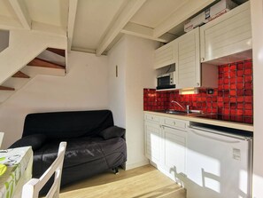 Cozinha compacta com armários brancos, uma parede de proteção vermelha e um sofá preto.