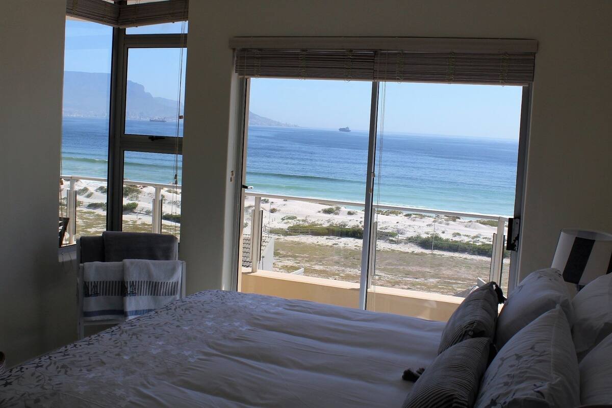 Een slaapkamer met een groot bed, uitzicht op het strand en een balkon met uitzicht op de oceaan.