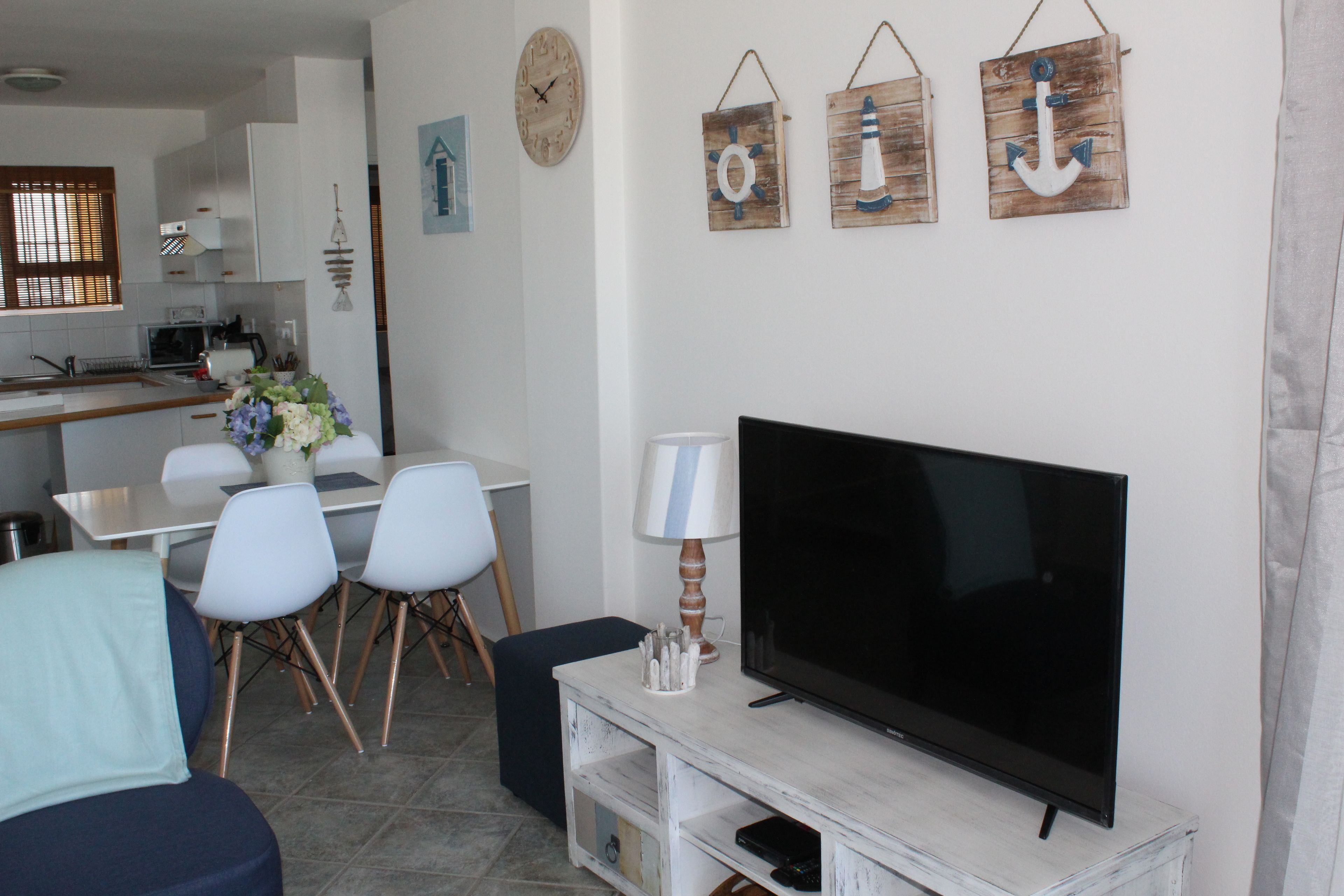 Un salón con televisor de pantalla plana, mobiliario blanco y decoración de temática náutica.