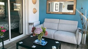 A living room with a grey sofa, a coffee table with magazines, a vase of flowers, and a large mirror on the wall.