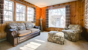 A cozy living room with wooden walls, a brown leather sofa, a patterned armchair, and a matching ottoman. - The Cottage an urban retreat. (Minneapolis)