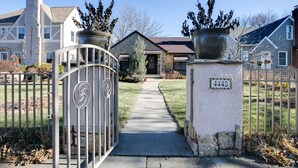 A gated driveway leading to a house with a stone facade, a number plaque, and large potted plants. - The Cottage an urban retreat. (Minneapolis)