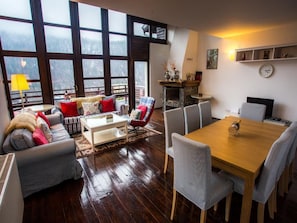 Una sala de estar acogedora con un conjunto de sofá, una mesa de centro y una mesa de comedor con sillas. Hay una chimenea y un ventanal con vistas al exterior.