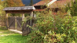 Une maison rustique en bois, surmontée d’un toit en métal, entourée d’une végétation luxuriante et avec des montagnes en toile de fond.