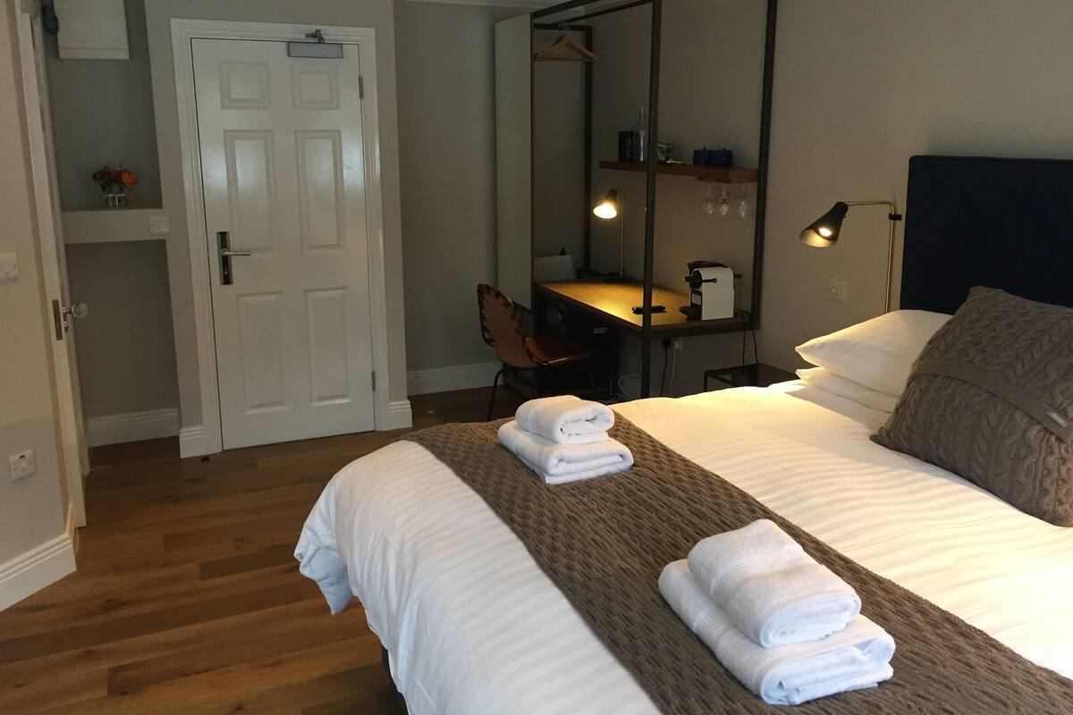 Habitación de hotel con cama, escritorio, silla, espejo y armario.