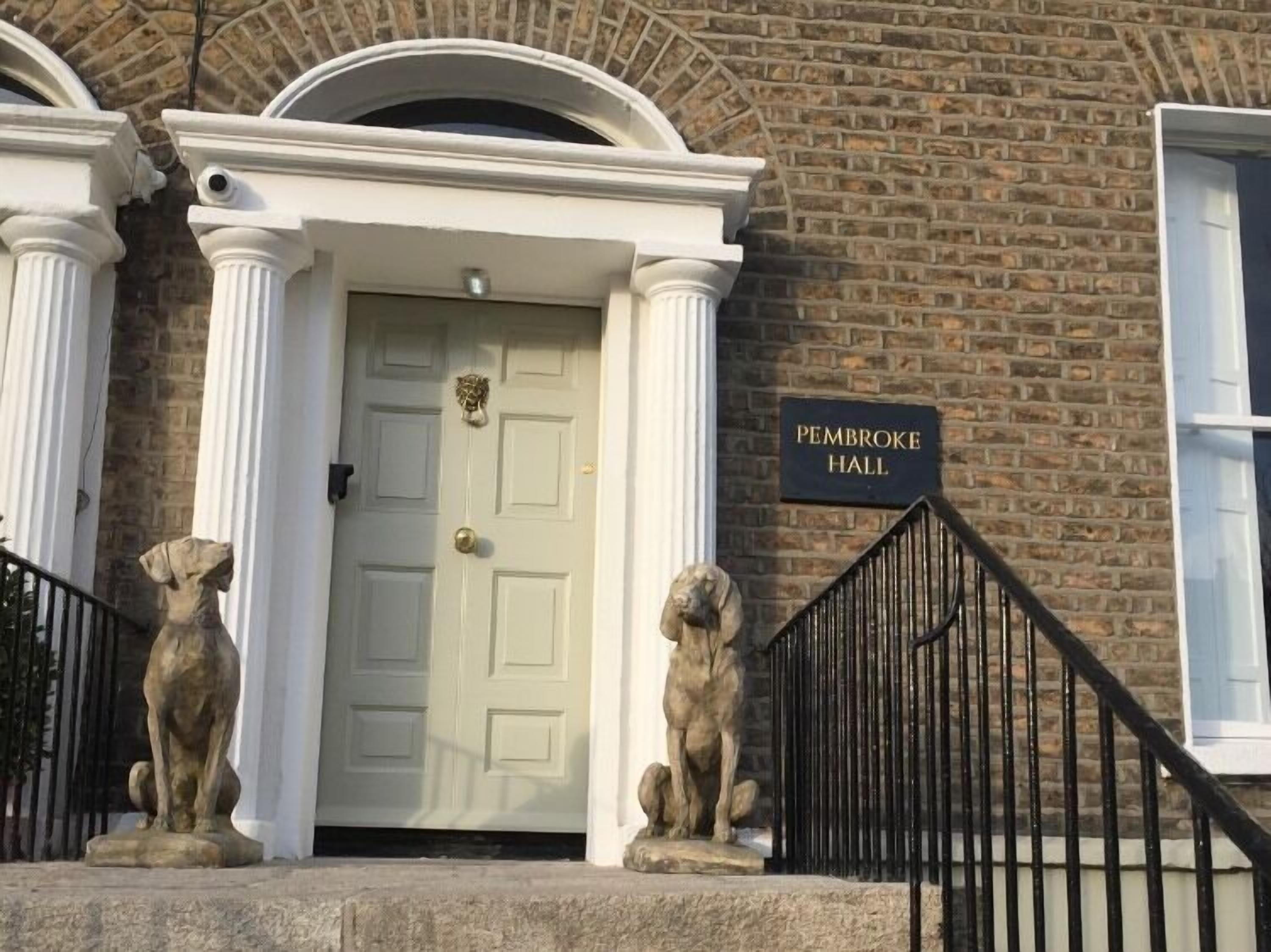 L'ingresso di un edificio con una porta bianca, due statue di leoni in pietra e un cartello con la scritta "Pembroke Hall".
