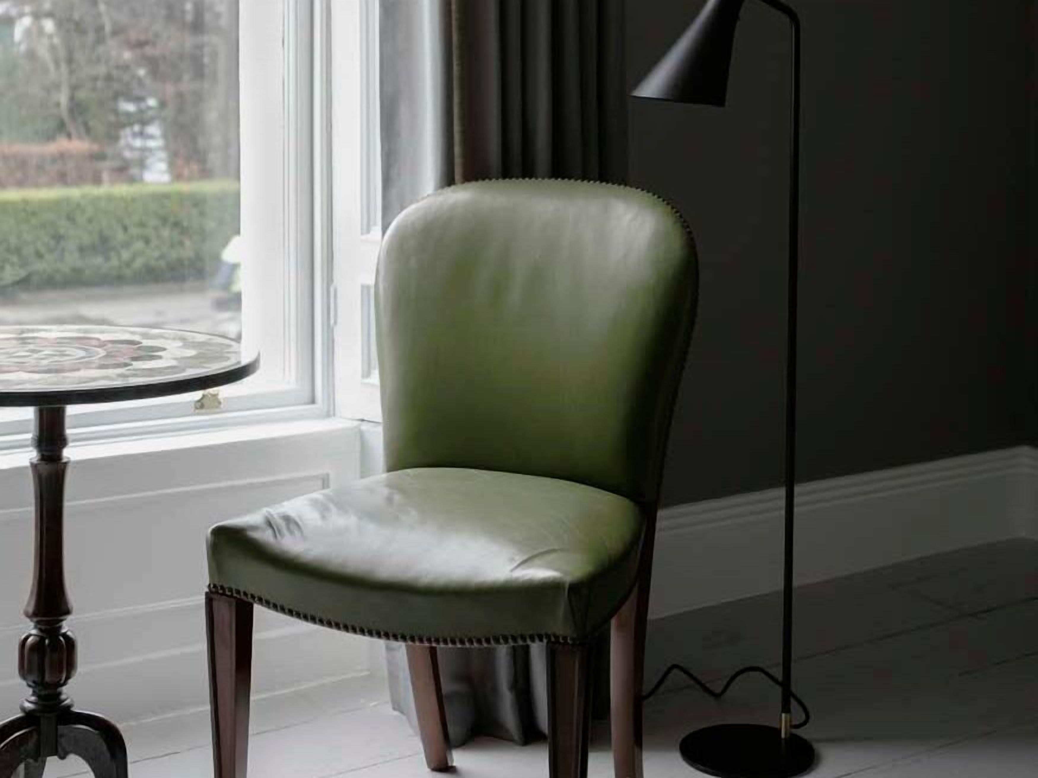 A green leather chair with a high backrest and a cushioned seat, positioned next to a round table with a glass top.