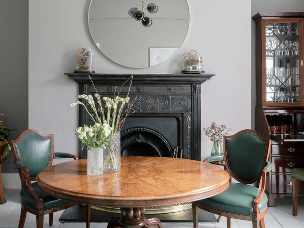 Un comedor con una mesa redonda, dos sillas, una chimenea y un espejo en la pared.