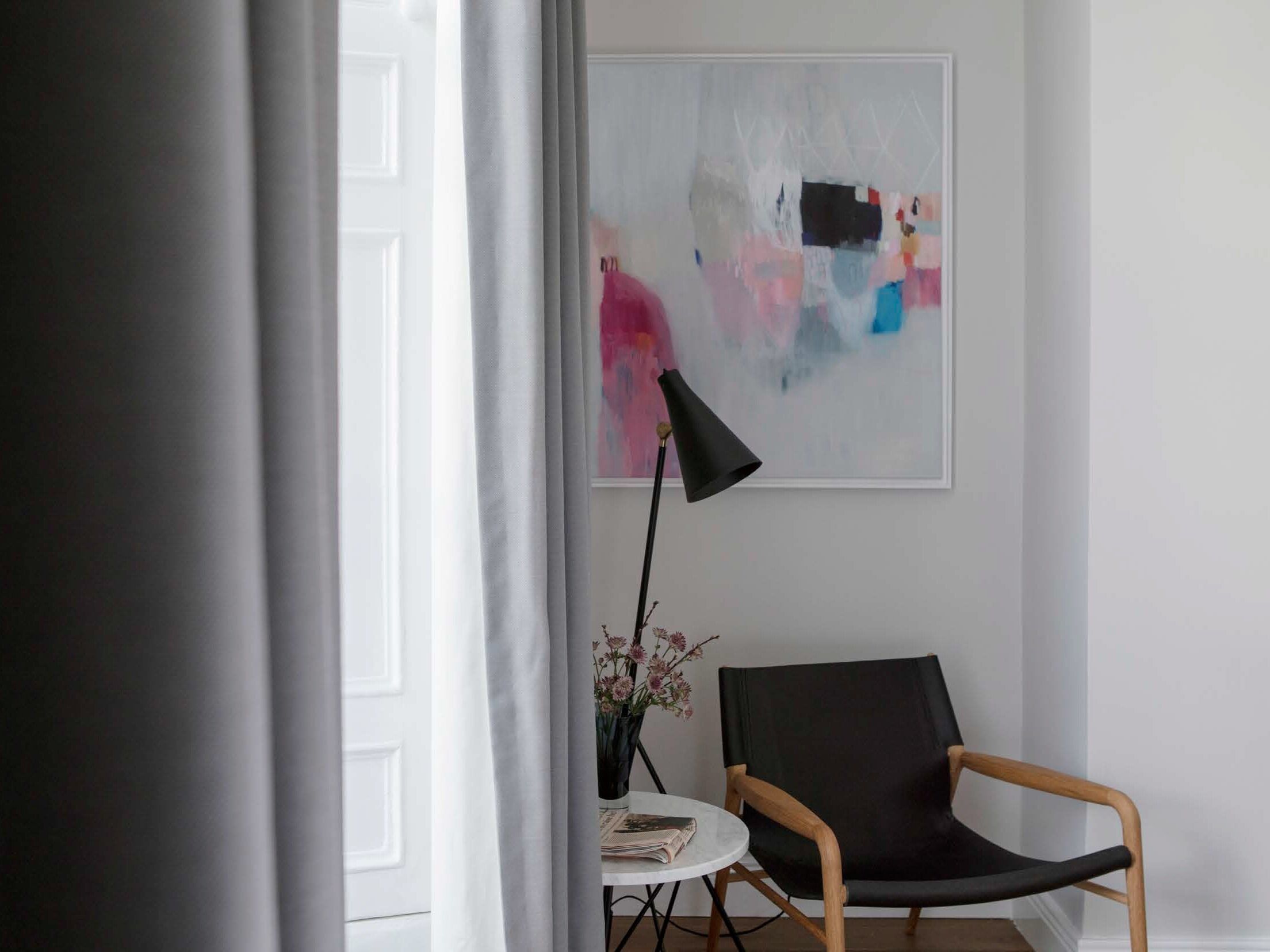 Una stanza con una sedia nera, un tavolino con un vaso di fiori e un quadro appeso al muro.