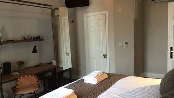 Una habitación de hotel con una cama, un escritorio con silla, un televisor montado en la pared y una puerta.