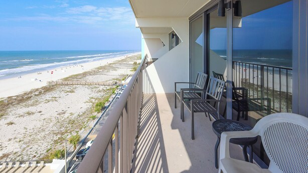 Een balkon met uitzicht op het strand en de oceaan. Er staan stoelen en een tafel op het balkon.