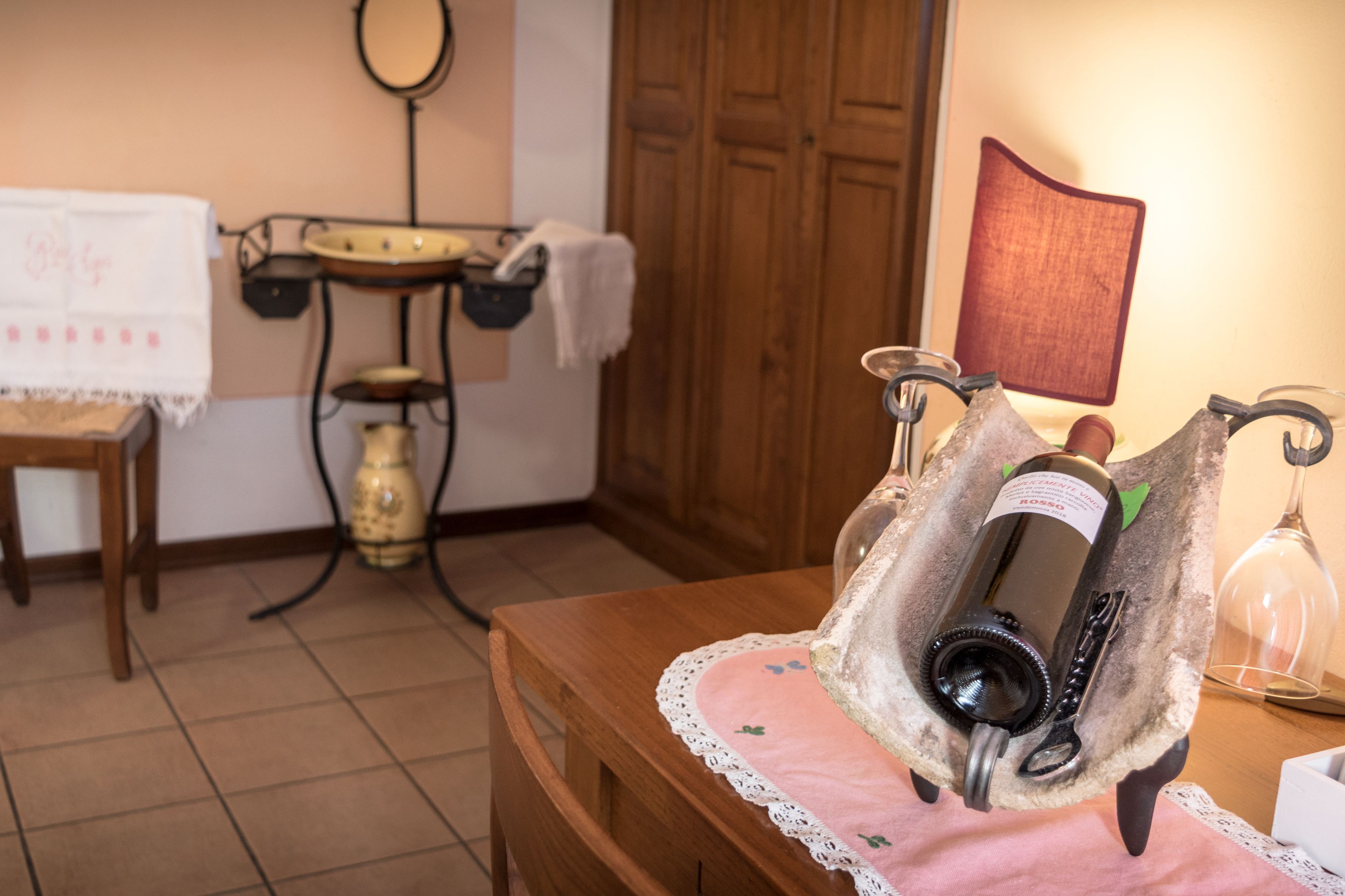 A wooden table with a bottle of wine, a wine opener, and a glass on a pink cloth.