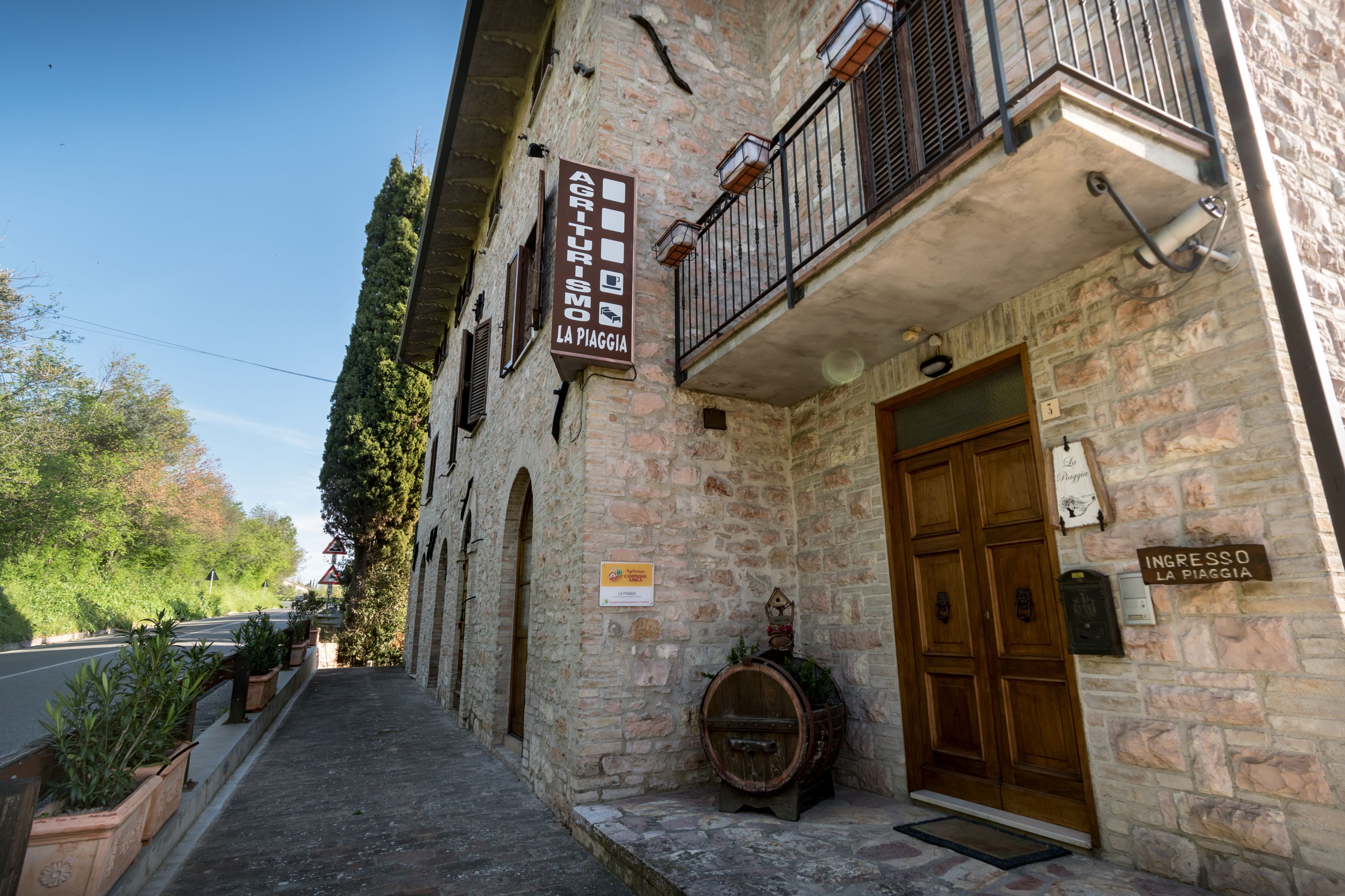Un edificio de piedra con puerta de madera y un balcón. Hay un cartel en la pared que dice "Agriturismo La Piaggia".