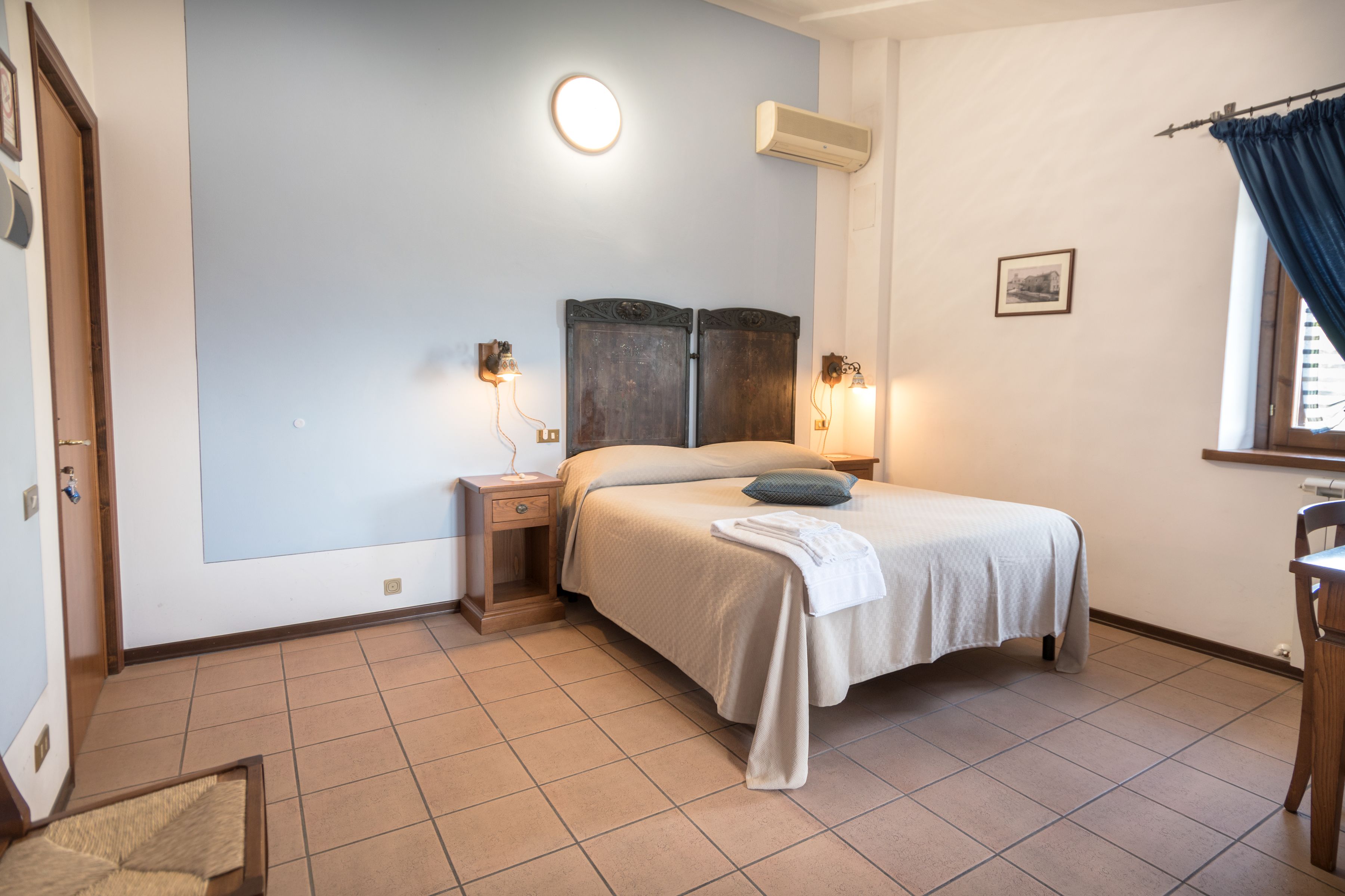 Une chambre à coucher comprenant un lit, des tables de chevet, un climatiseur fixé au mur et une fenêtre avec des rideaux.