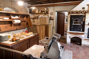 Una cocina con un arco de piedra, estantes de madera, un horno de pizza y una máquina para cortar fiambres.