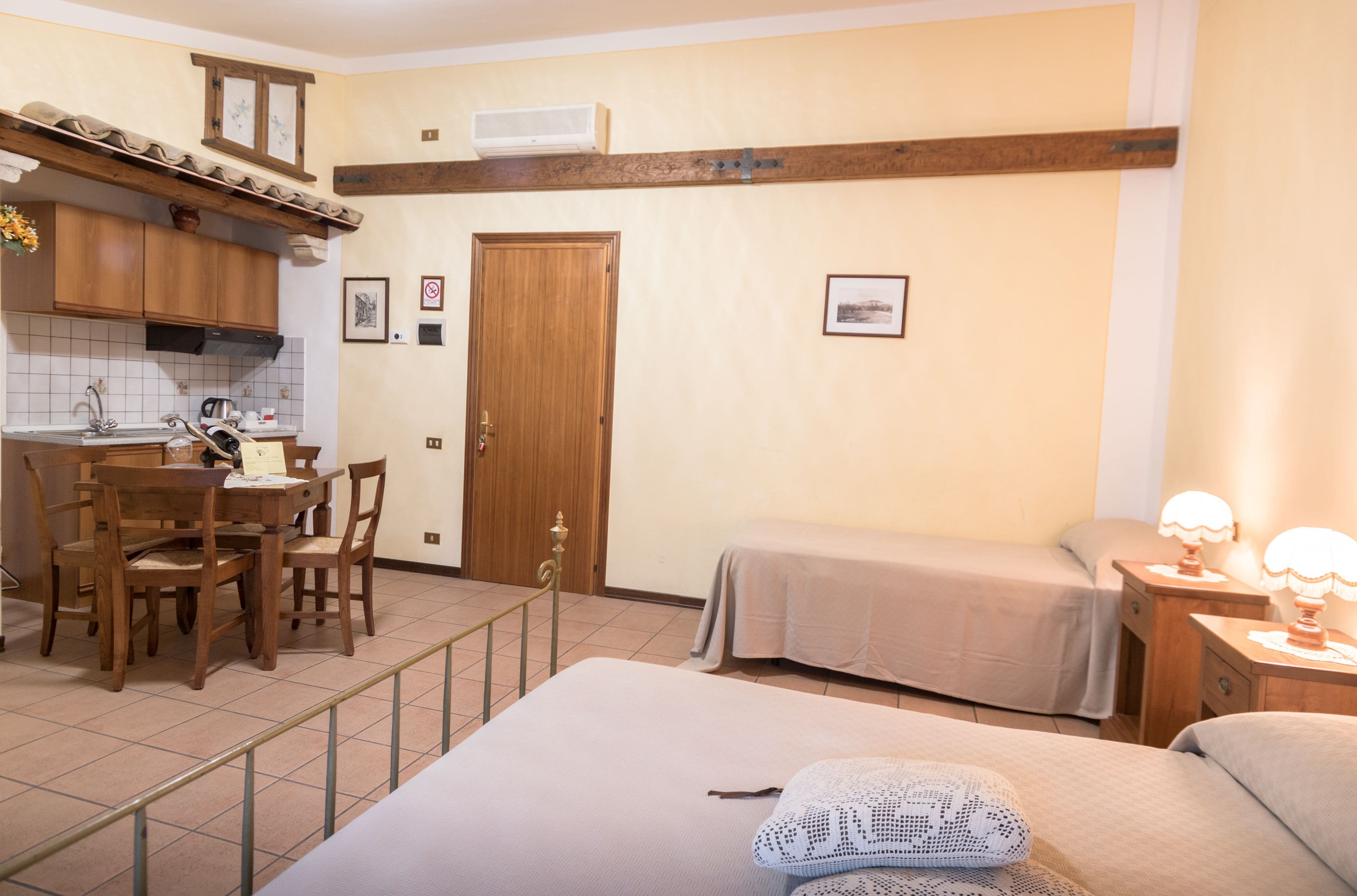 A compact hotel room with a kitchenette, a dining area, and two single beds.