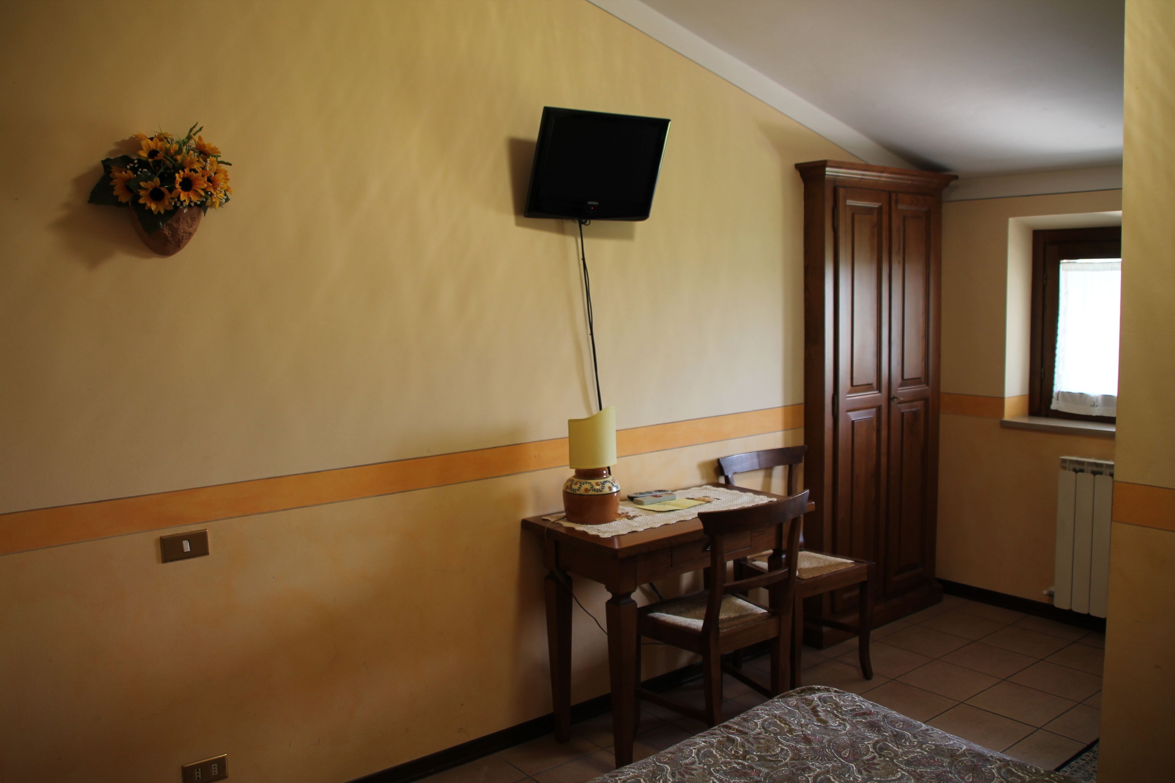 A room with a desk, chair, TV mounted on the wall, and a cabinet.
