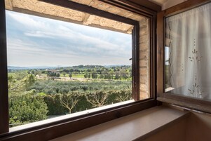 Una ventana con vistas a un paisaje rural, que incluye árboles y colinas distantes.