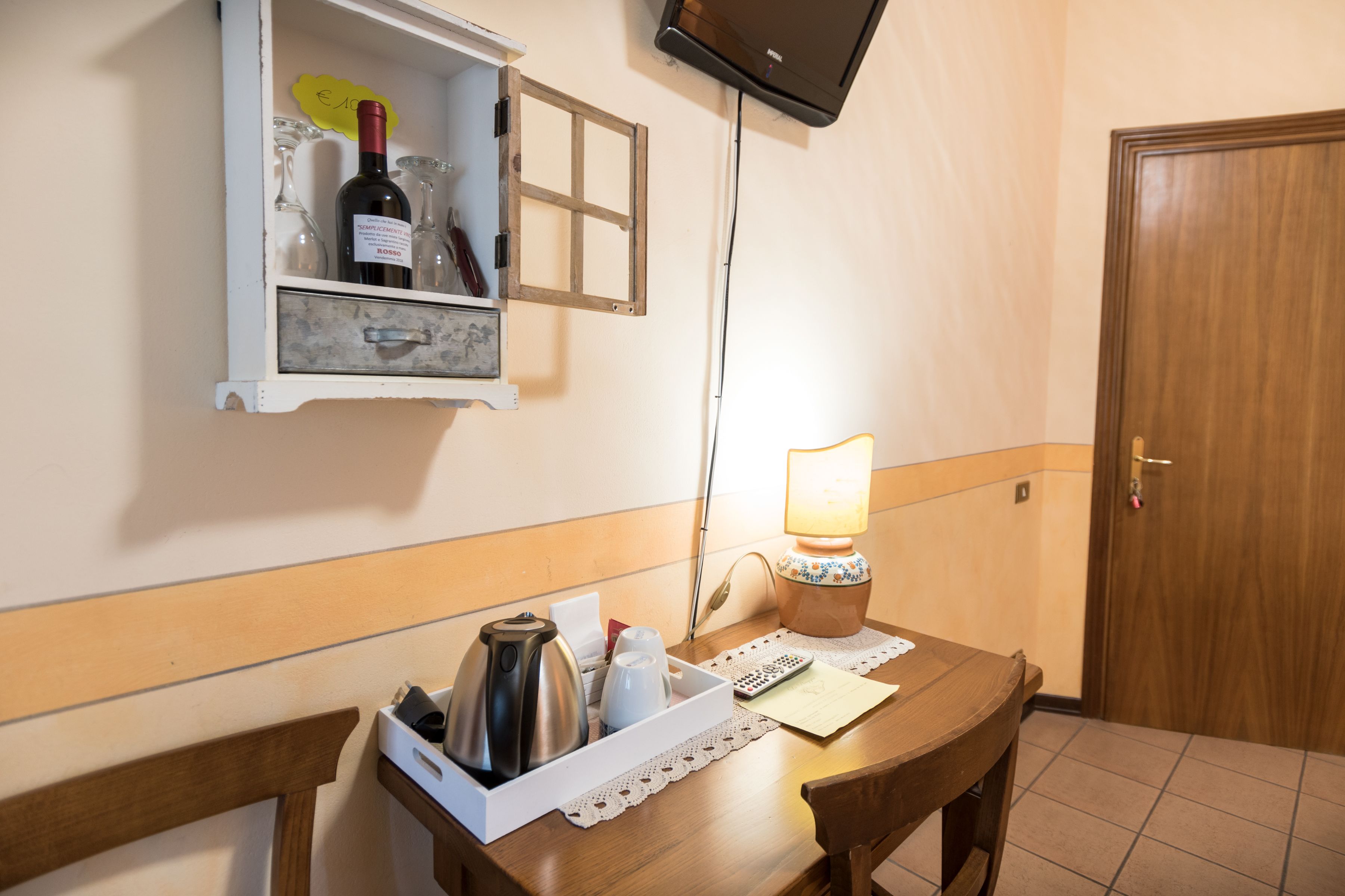 A hotel room with a wooden table, a minibar, a television mounted on the wall, and a wooden door.