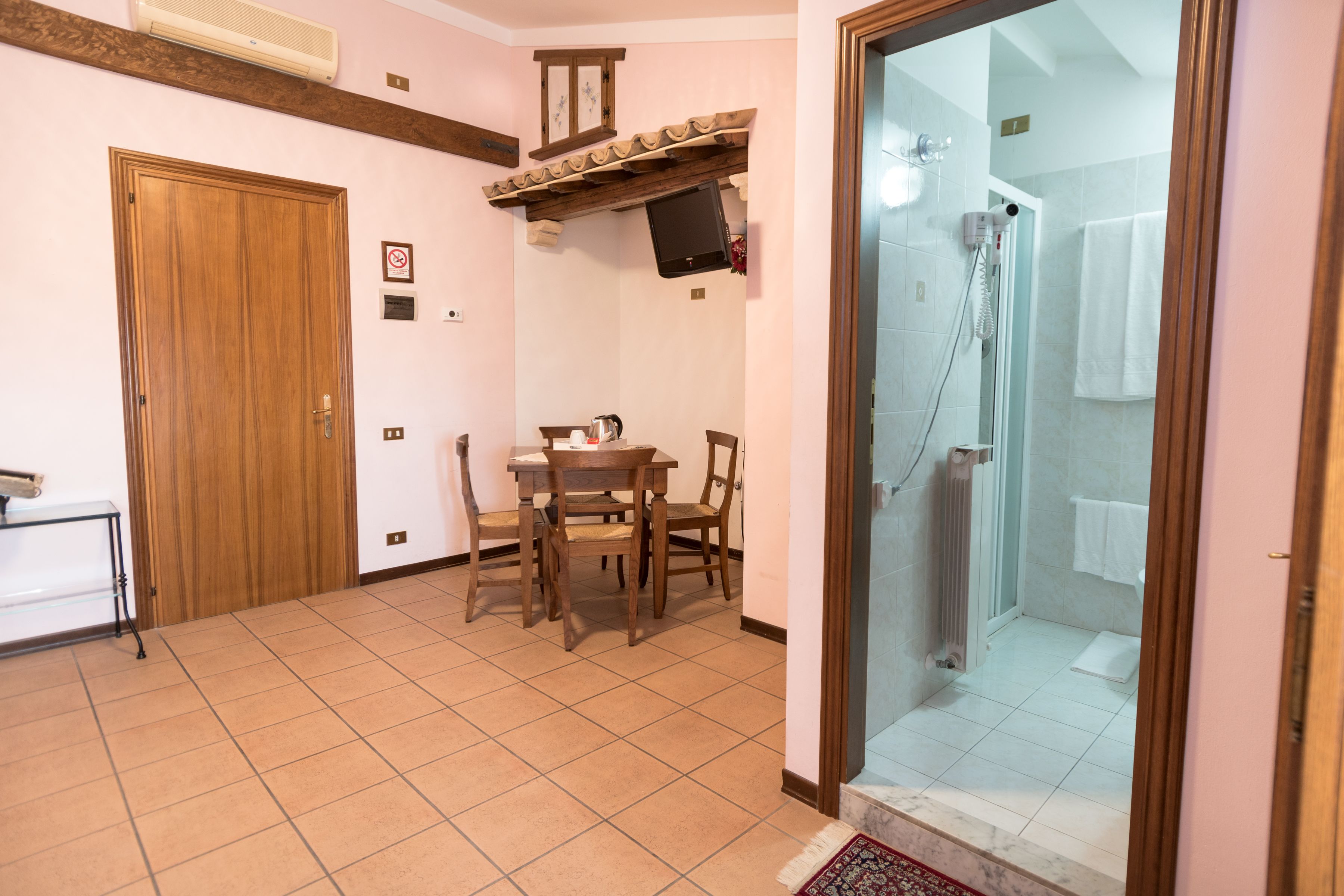 A room with a wooden door, a dining table with chairs, a mounted TV, and a shower area with a glass door.