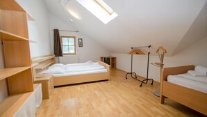 Een ruime slaapkamer op zolder met een schuine kap, twee bedden, houten vloeren en een dakraam.