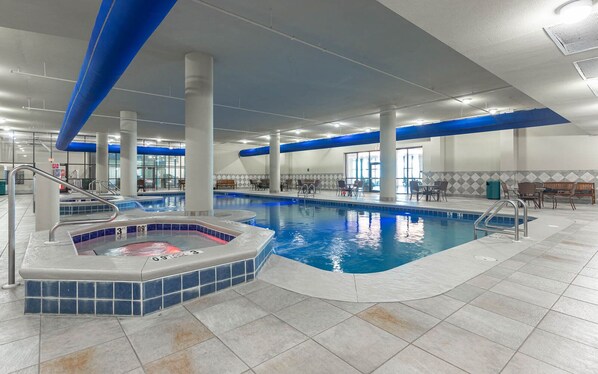 An indoor swimming pool with a hot tub, tiled flooring, and seating areas.