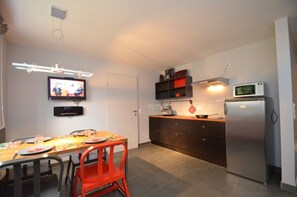 Una cocina compacta con una mesa de comedor, sillas, un televisor, un microondas y un refrigerador.