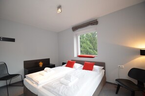 Een hotelkamer met een groot bed, een raam met uitzicht op bomen, een nachtkastje en een stoel.