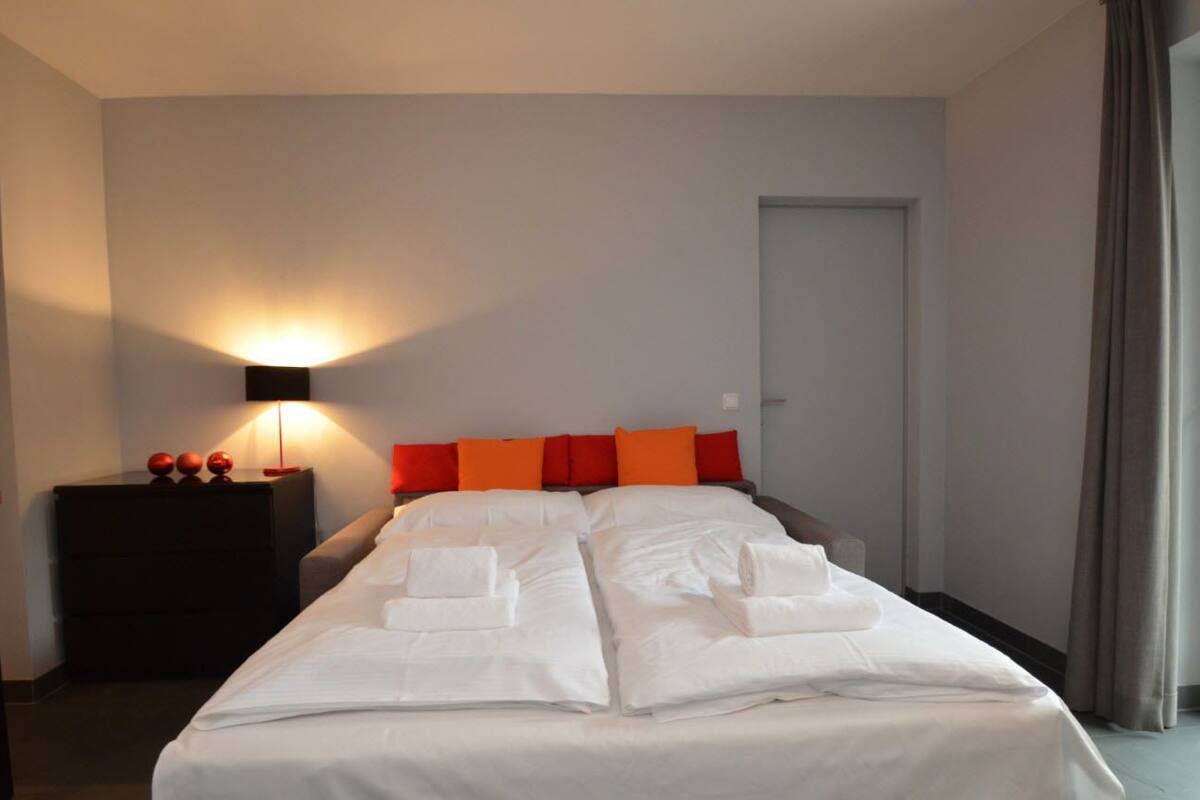 Una habitación de hotel con una cama grande, una mesita de noche con lámpara y una puerta.