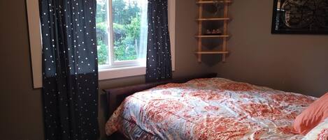 Un dormitorio con cama, ventana con cortinas, escalera y estante en la pared.